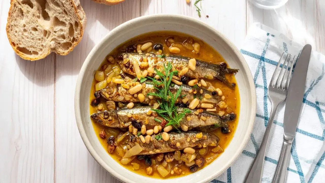 Sarde in saor, un piatto veneziano con sarde, cipolle, pinoli e uvetta, servito in una ciotola con pane rustico.