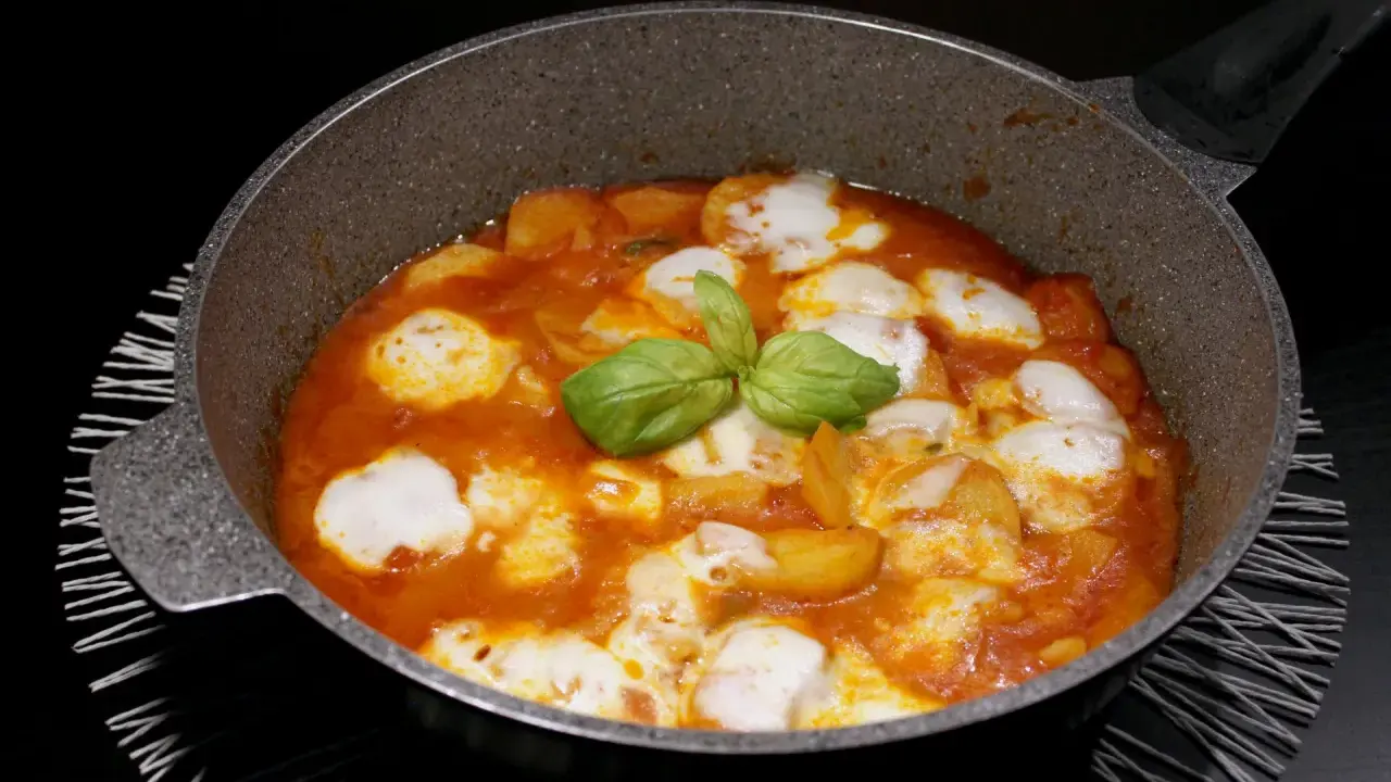 Patate alla pizzaiola in padella, con mozzarella filante e basilico fresco. Un piatto gustoso e invitante.