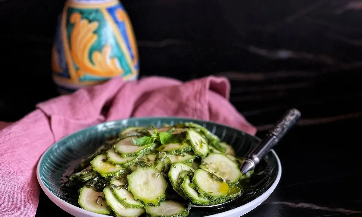 Fetta di zucchine marinate crude condite con erbe aromatiche e olio, servite su un piatto verde.