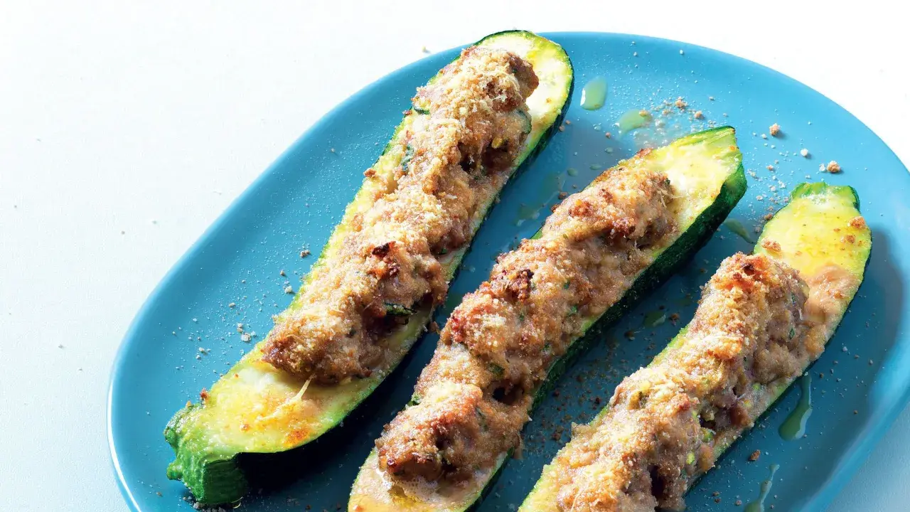 Tre zucchine ripiene, dorate e gratinate, servite su un piatto blu. Un piatto invitante e saporito.