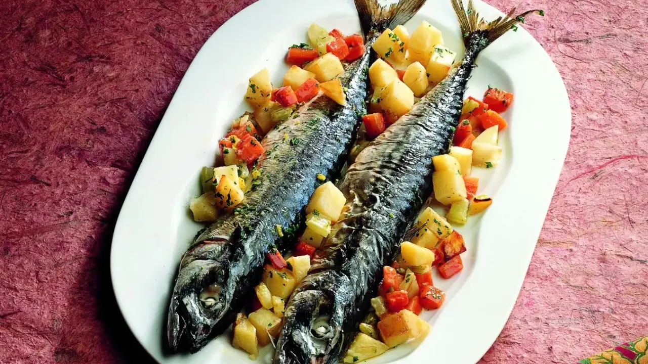 Due filetti di sgombro al forno, cotti alla perfezione, serviti con patate e carote a cubetti su un piatto bianco.