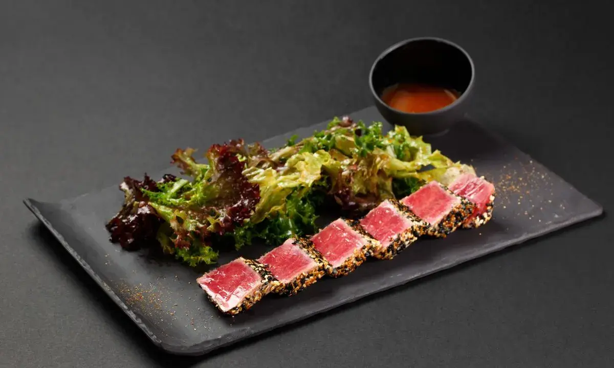 Tataki di tonno scottato, servito con insalata fresca e una ciotolina di salsa.
