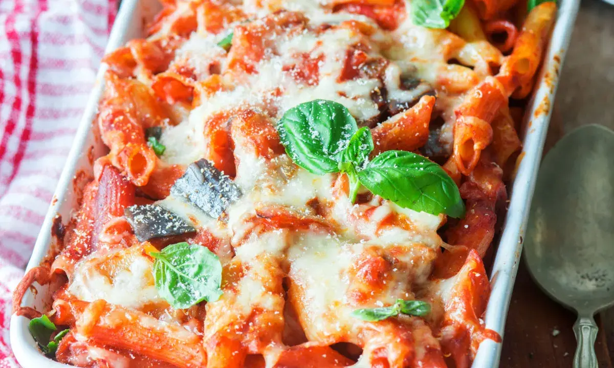 Penne al forno con melanzane, pomodoro e abbondante formaggio filante, guarnite con basilico fresco.