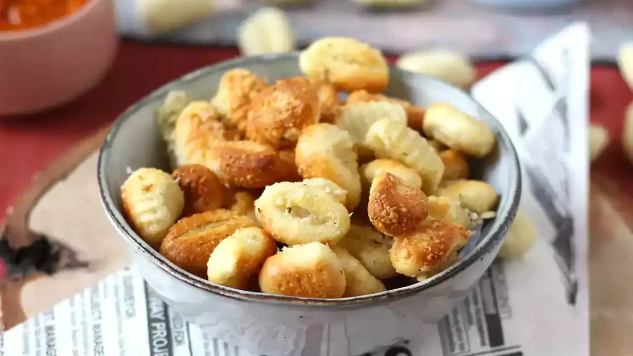 Gnocchi dorati e croccanti in friggitrice ad aria, serviti in una ciotola su carta di giornale.