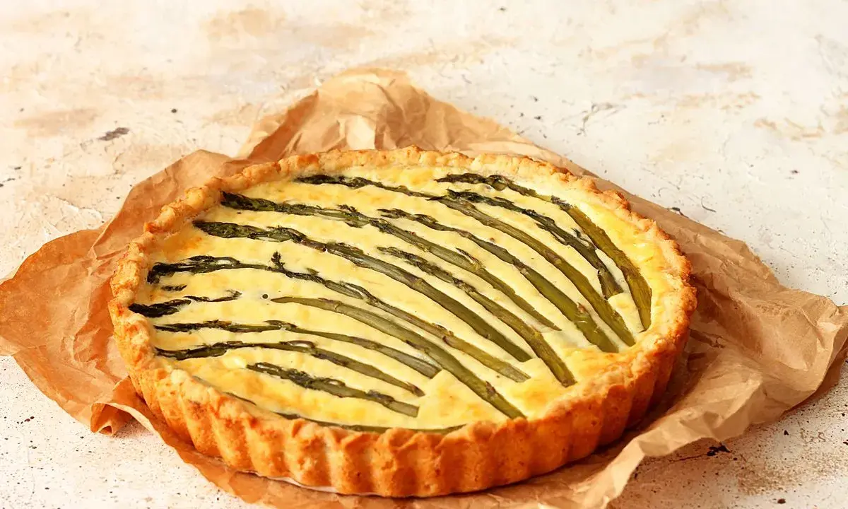 Torta salata asparagi con crosta dorata e ripieno cremoso, decorata con asparagi freschi disposti a raggiera.
