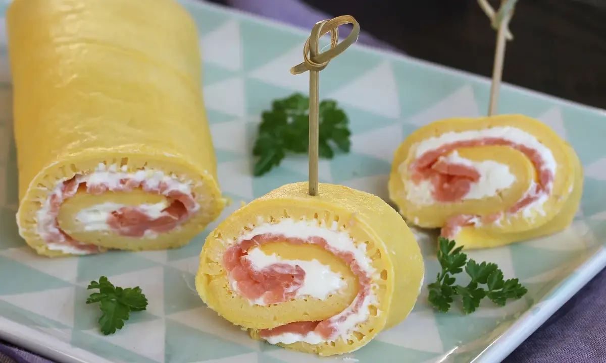 Rotolo di frittata ripieno di salmone affumicato e formaggio cremoso, guarnito con prezzemolo. Un antipasto elegante e gustoso.