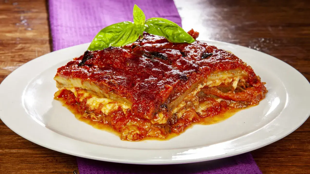 Una fetta di parmigiana di melanzane napoletana, ricca e saporita, guarnita con basilico fresco.
