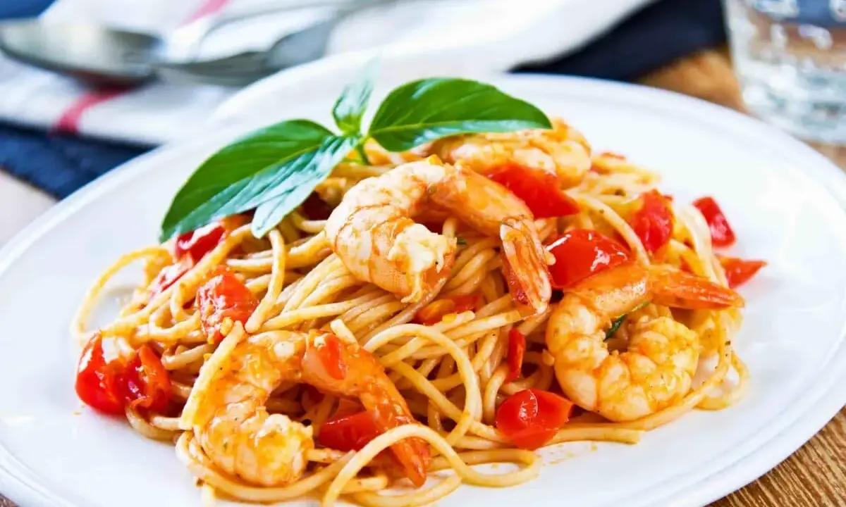 Un piatto invitante di spaghetti con gamberetti succulenti e pomodorini freschi, guarnito con basilico.