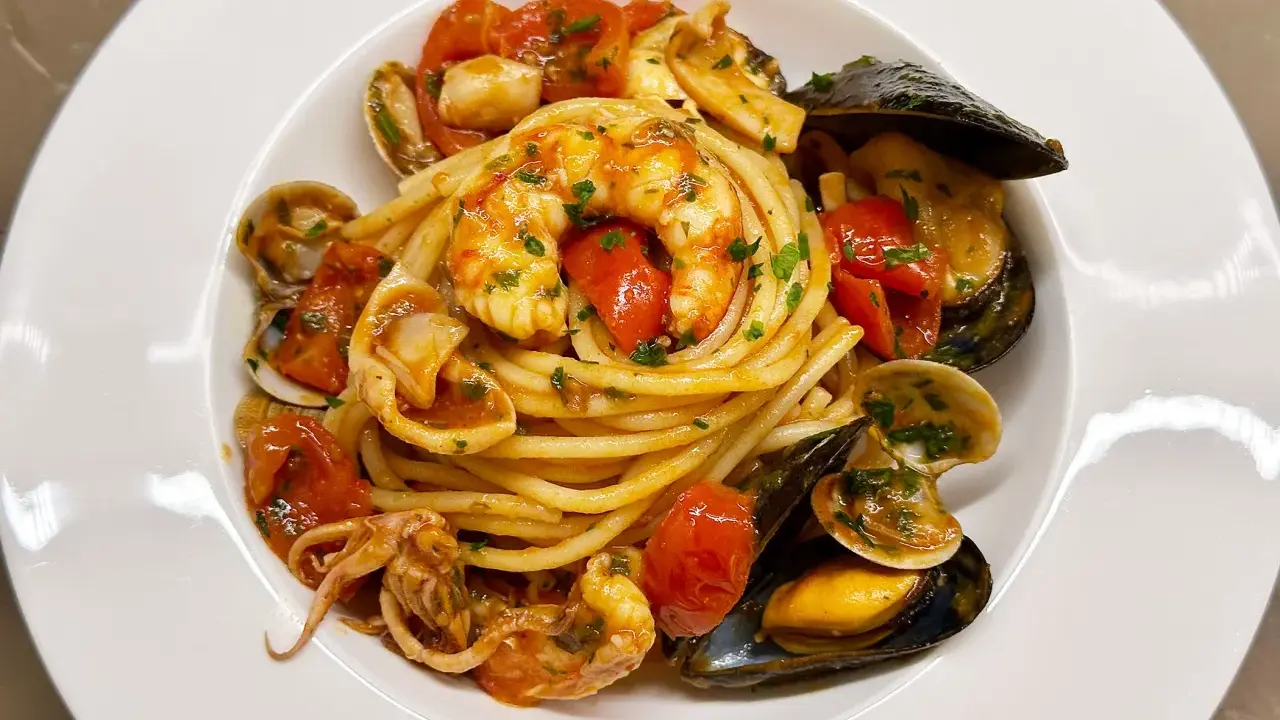 Un invitante piatto di spaghetti allo scoglio, con gamberi, cozze, vongole e calamari, condito con pomodorini e prezzemolo.
