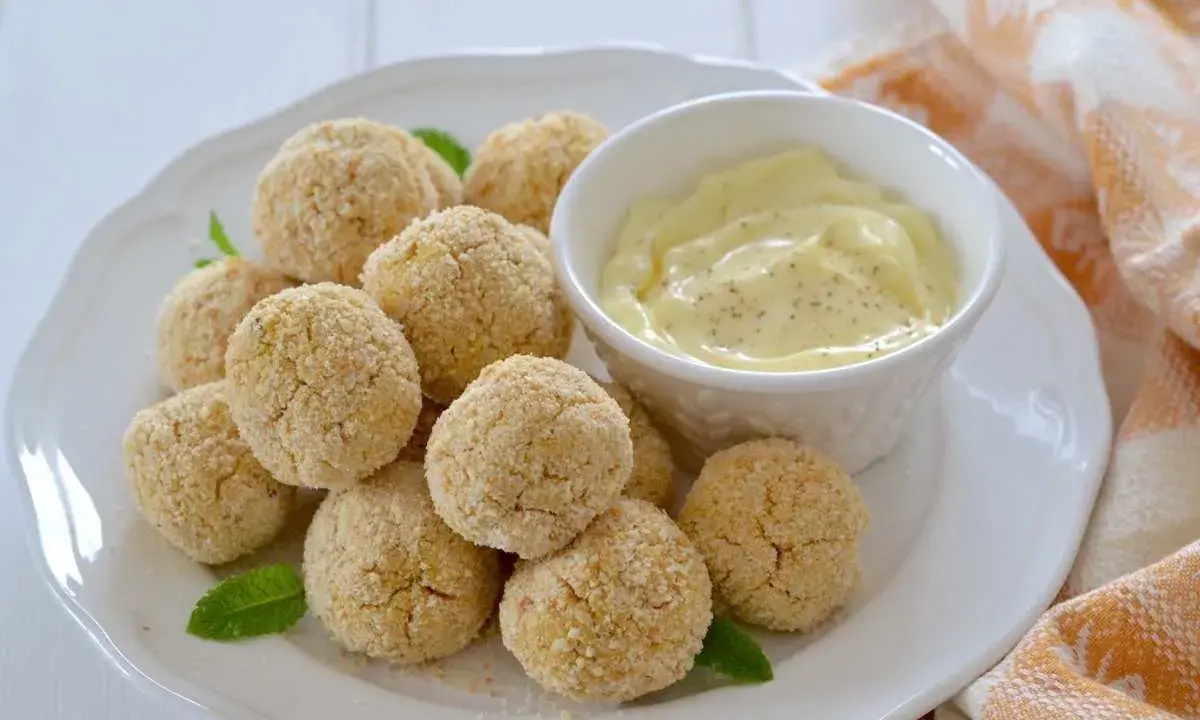 Polpette di ceci al forno dorate e croccanti, servite su un piatto bianco con una ciotolina di salsa cremosa e foglie di menta.