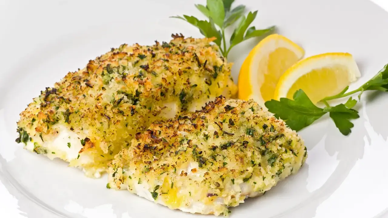 Delizioso merluzzo al forno con crosta croccante di erbe e pangrattato, guarnito con spicchi di limone e prezzemolo fresco.