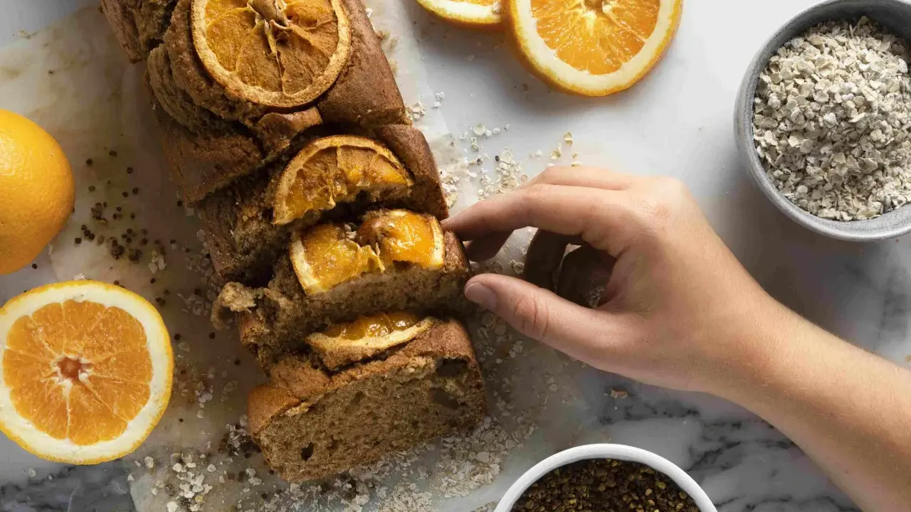 Un profumato plumcake all'arancia, uno dei tanti dolci senza glutine, pronto per essere gustato. Accanto, arance fresche e avena.