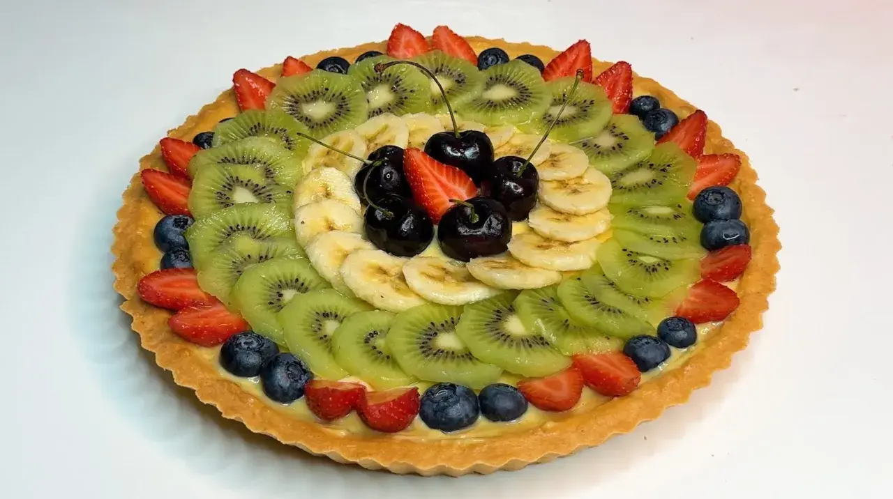 A fruit tart with kiwi, banana, strawberries, blueberries, and cherries on a custard filling.