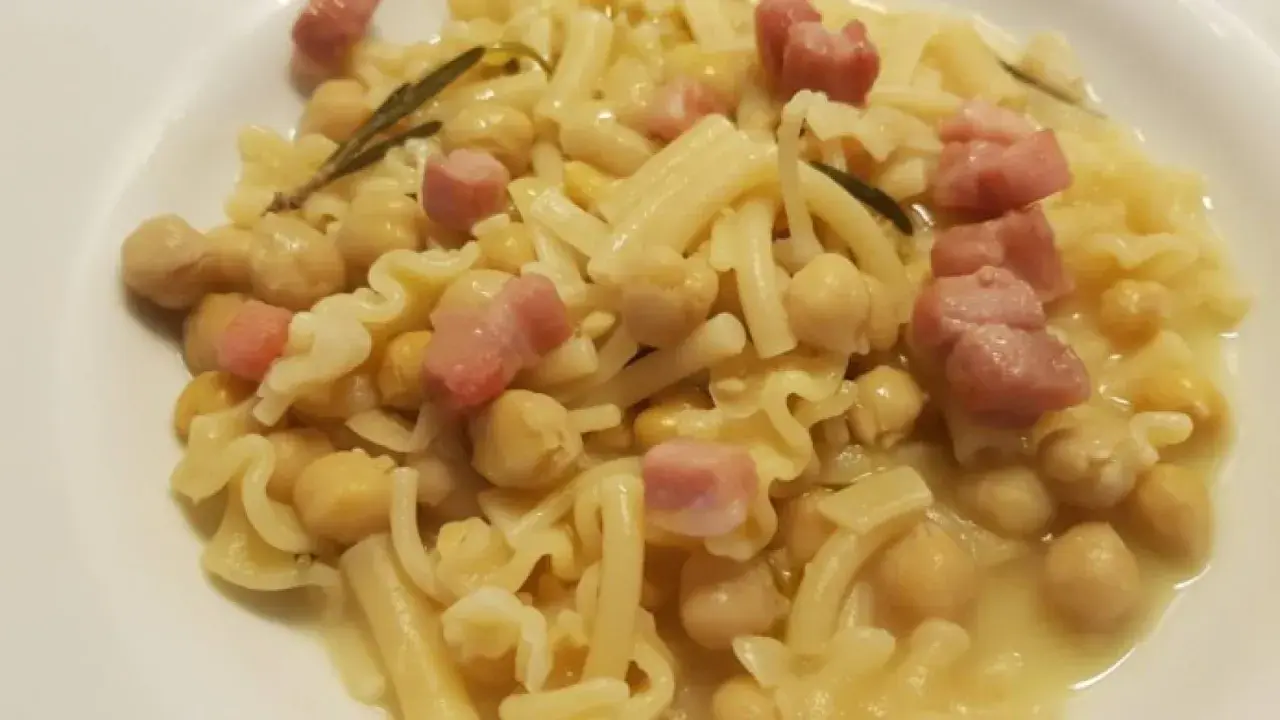 Un piatto di pasta e ceci in scatola, arricchito da cubetti di pancetta e un rametto di rosmarino.