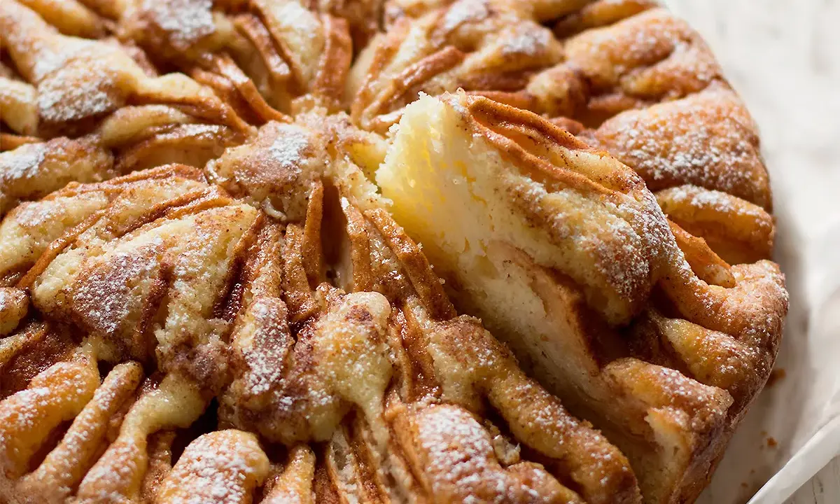 Una deliziosa torta di mele, cosparsa di zucchero a velo, con una fetta appena tolta che ne rivela la morbidezza.
