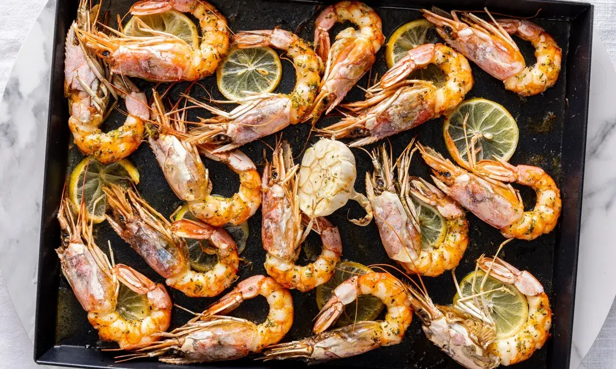 Gamberoni al forno dorati e succulenti, conditi con erbe aromatiche e spicchi di limone, pronti per essere gustati.