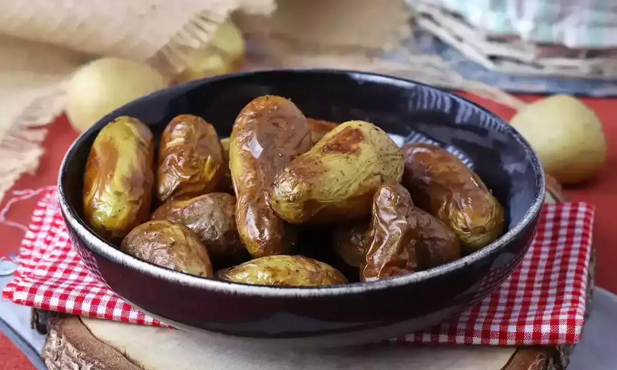 Patate novelle dorate e croccanti, appena sfornate dalla friggitrice ad aria, servite in una ciotola scura su un tagliere di legno.