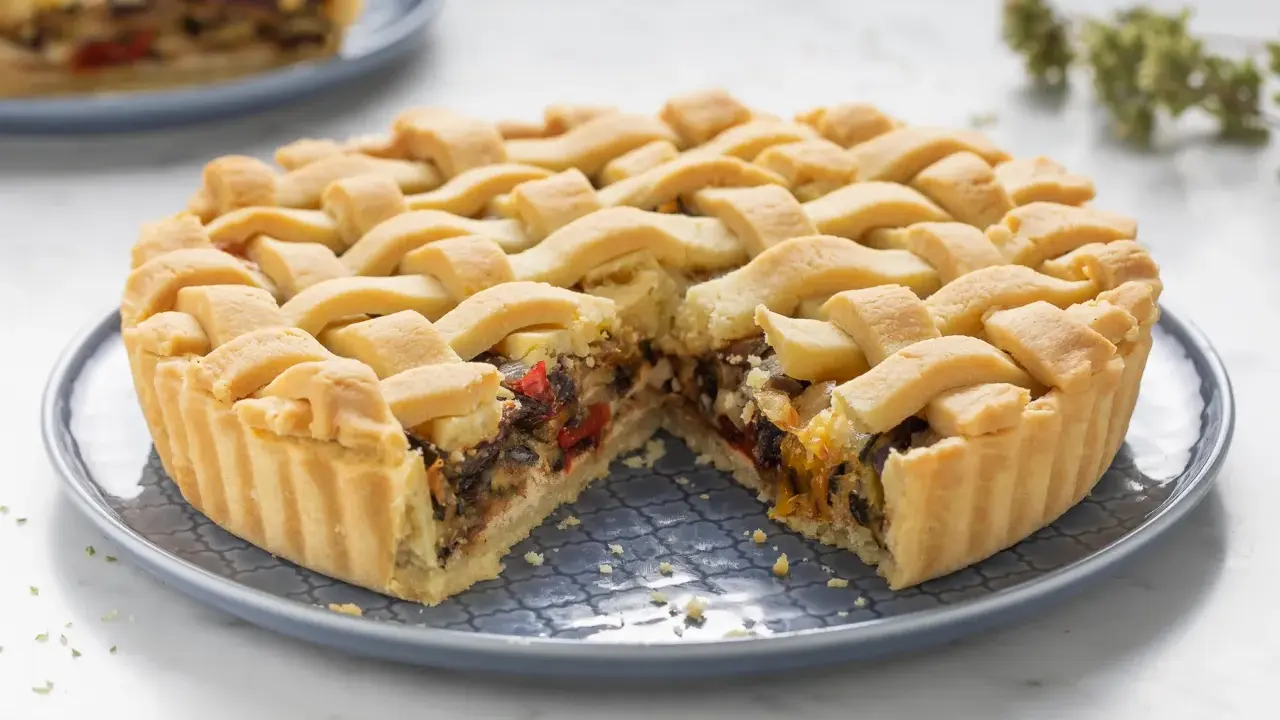 Una crostata morbida salata con verdure miste, peperoni e melanzane, ricoperta da una griglia di pasta dorata.