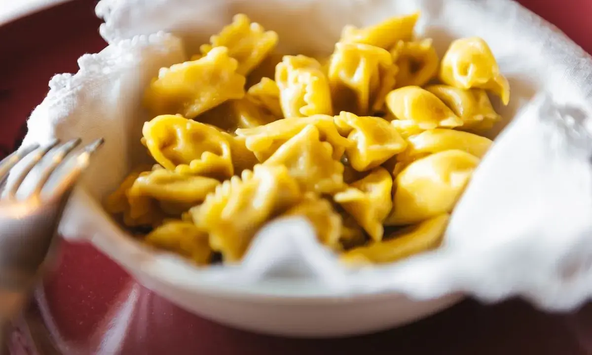 Un primo piatto invitante: tanti ravioli del plin dorati, serviti in una ciotola bordata di bianco.