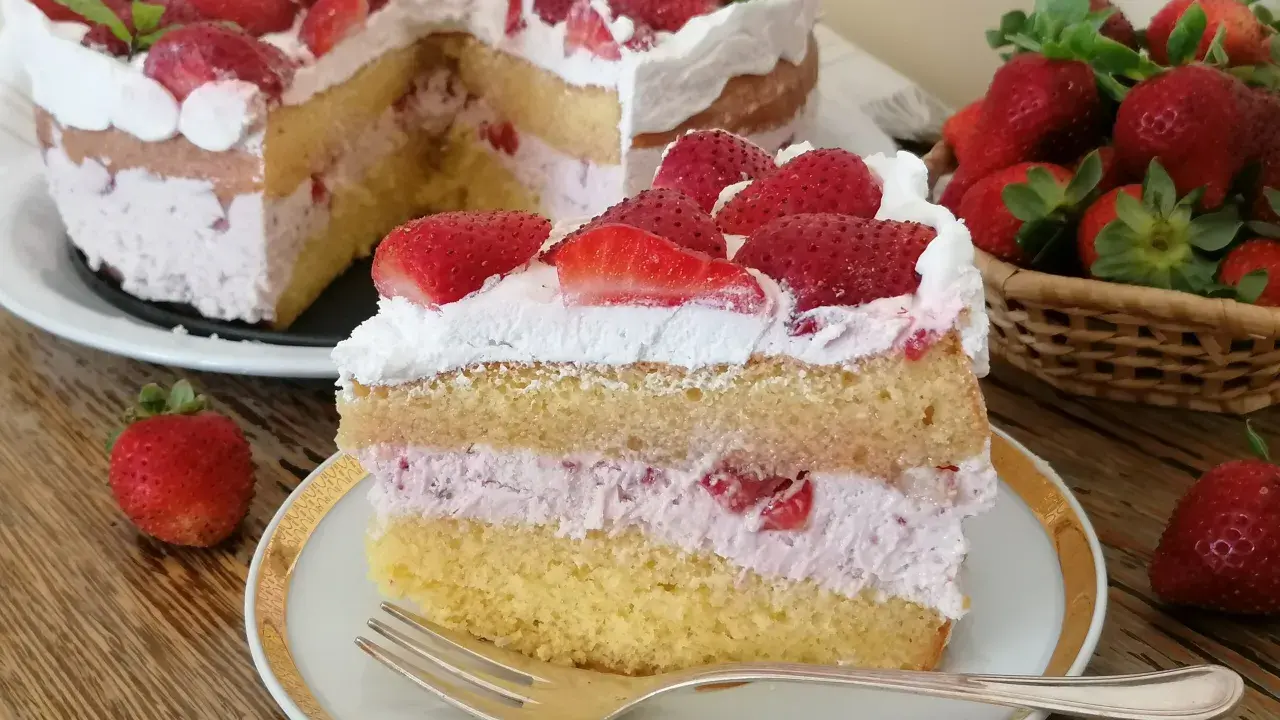 Una fetta di torta mascarpone e fragole, con strati di pan di spagna, crema rosa e fragole fresche, guarnita con panna e fragole.