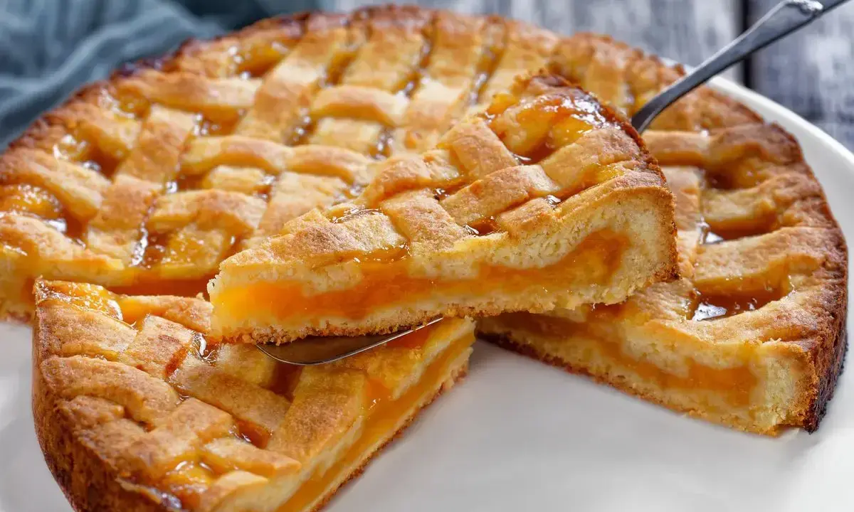 Deliziosa crostata senza glutine con ripieno di albicocche, una fetta sollevata da una paletta mostra la morbidezza.