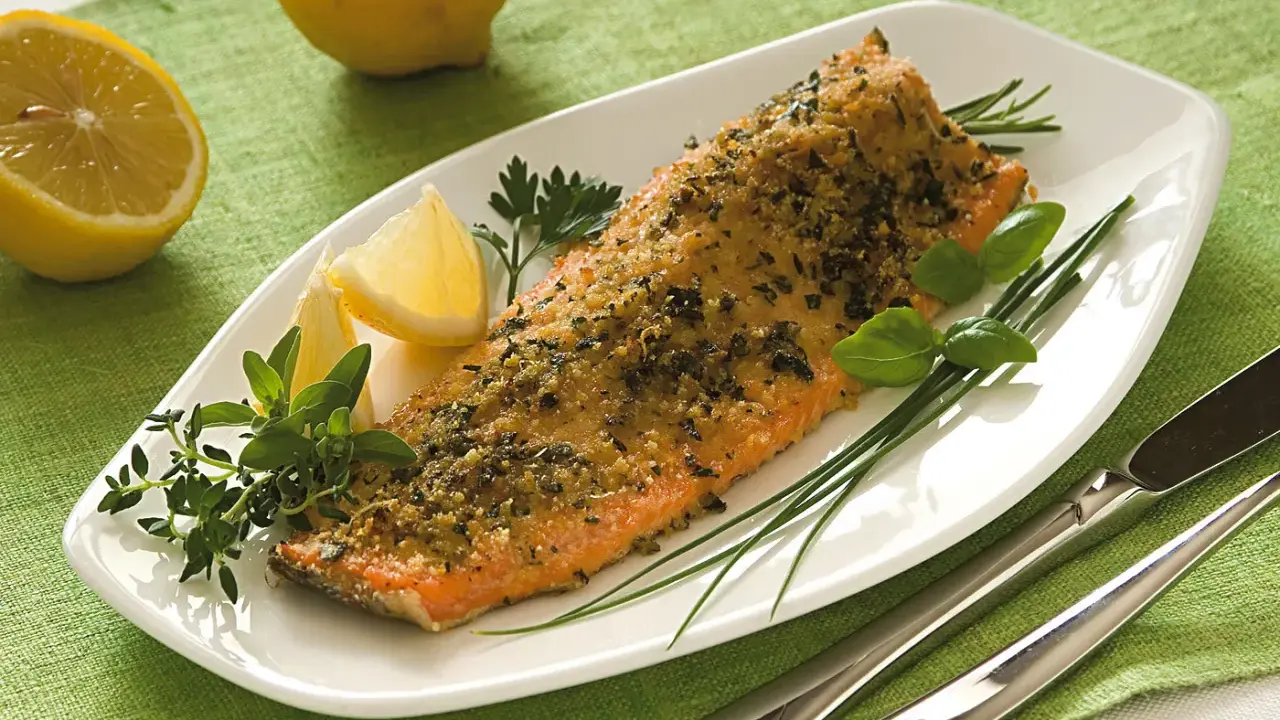 Deliziosa trota salmonata al forno, croccante e profumata, servita con limone e erbe aromatiche fresche.