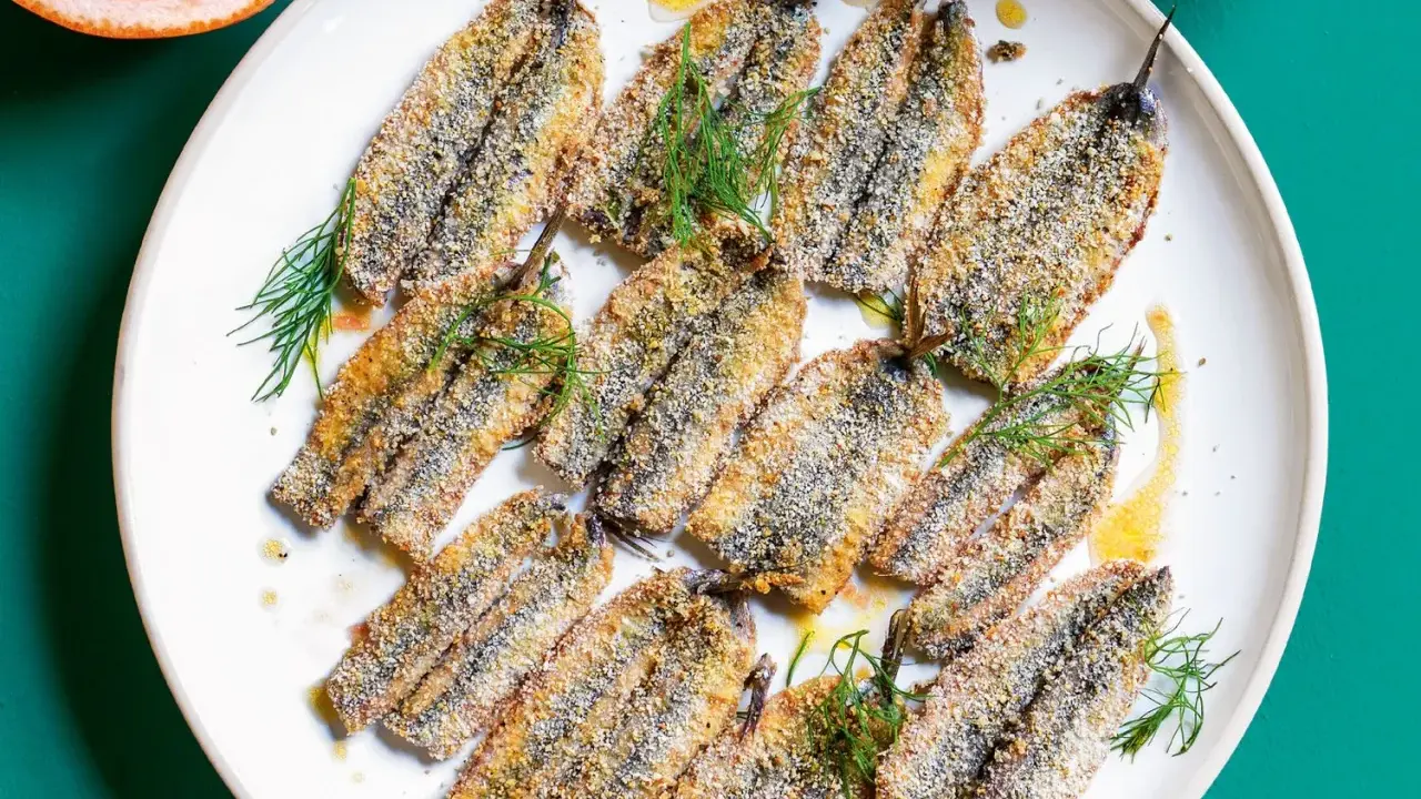 Piatto di alici al forno dorate e croccanti, guarnite con finocchietto fresco e un filo d'olio.