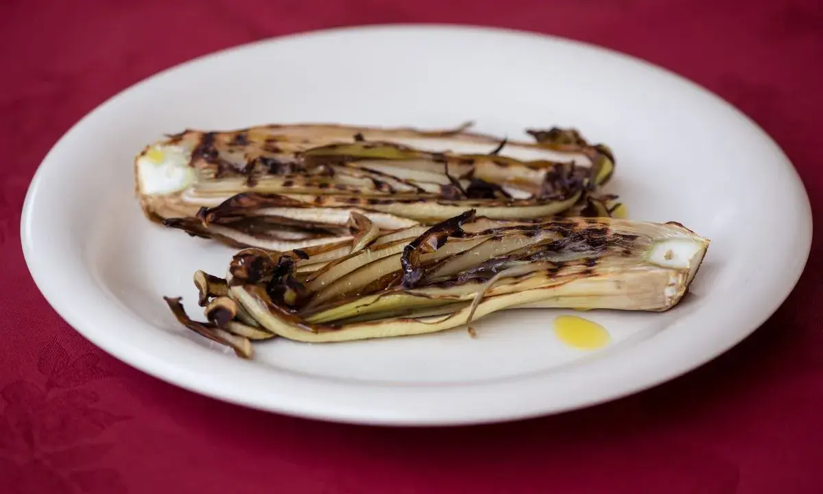 Radicchio in padella, grigliato e caramellato, servito su un piatto bianco con un filo d'olio.