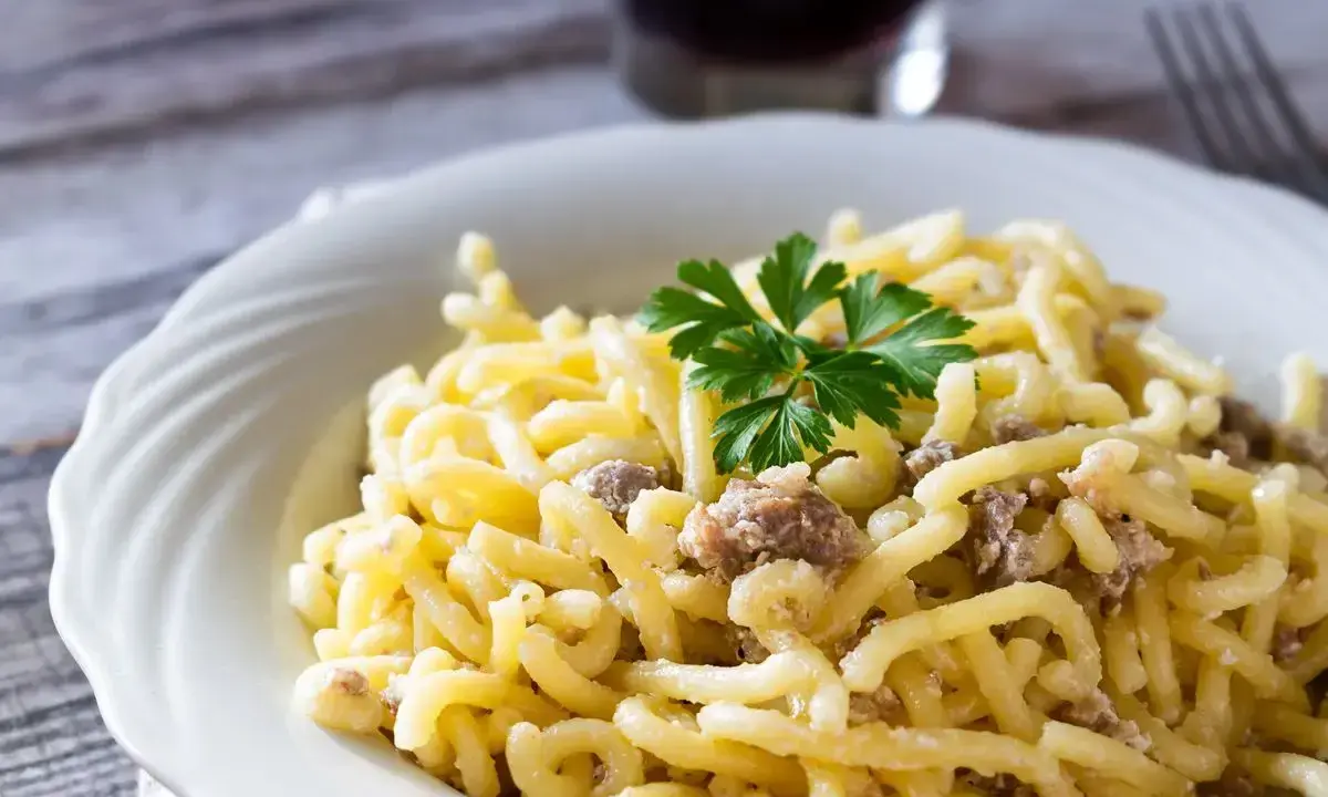 Piatto di pasta con salsiccia sbriciolata, condita con un sugo cremoso e guarnita con prezzemolo fresco.
