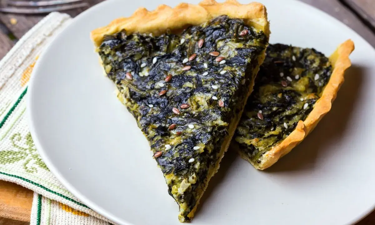 Fette di torta salata vegana con spinaci e semi di lino, su un piatto bianco.