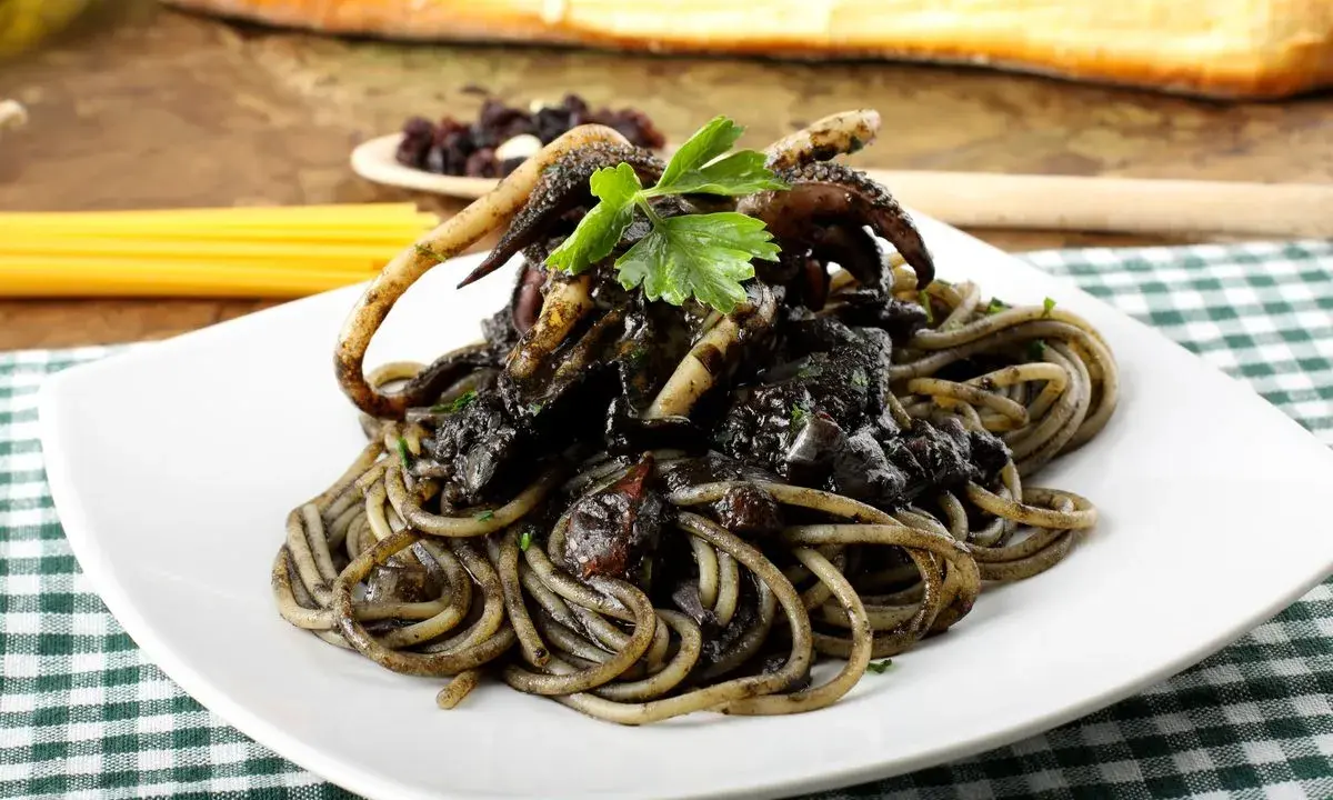 Un piatto invitante di spaghetti al nero di seppia, con tentacoli di calamaro e prezzemolo fresco, su una tovaglia a quadri verdi.