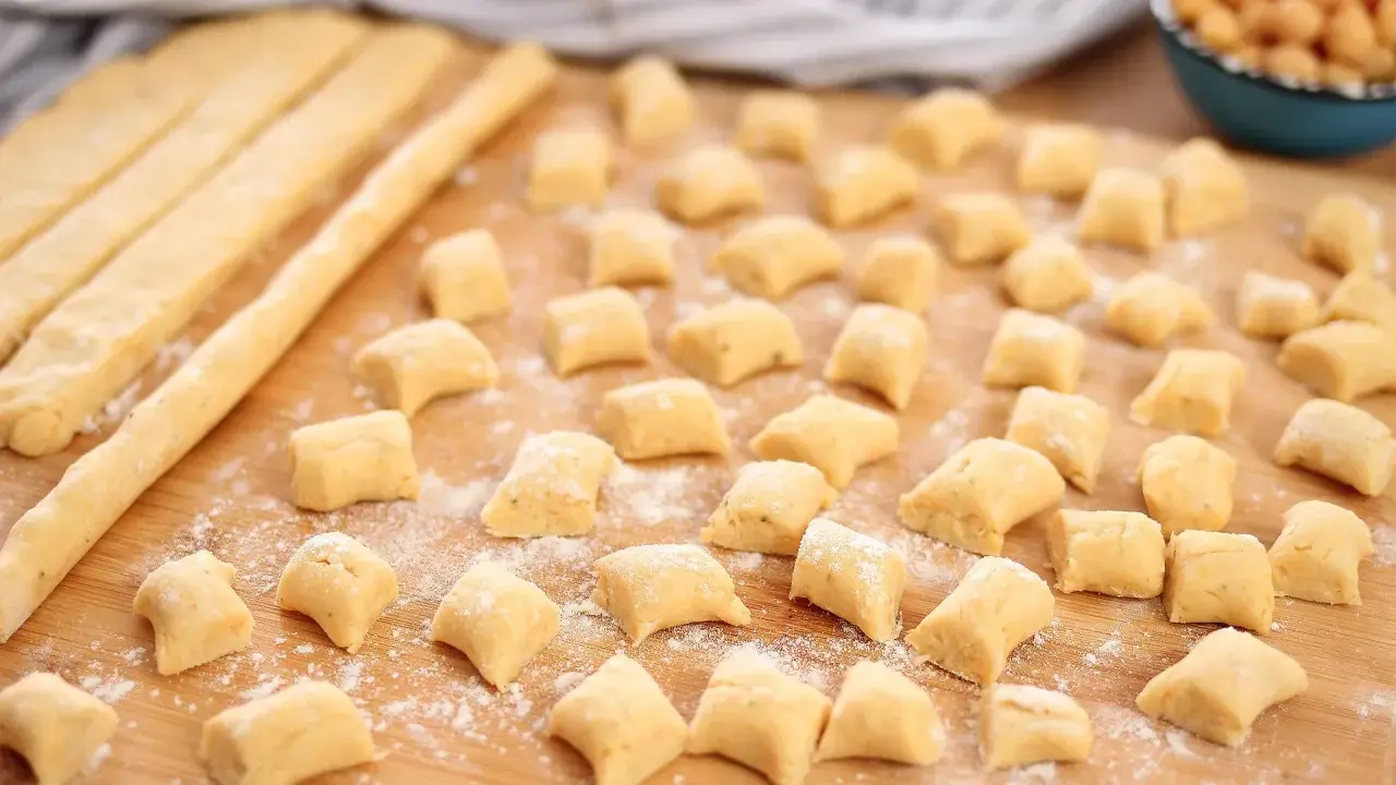 Piccoli gnocchi di ceci sparsi su un tagliere di legno, pronti per essere cotti.