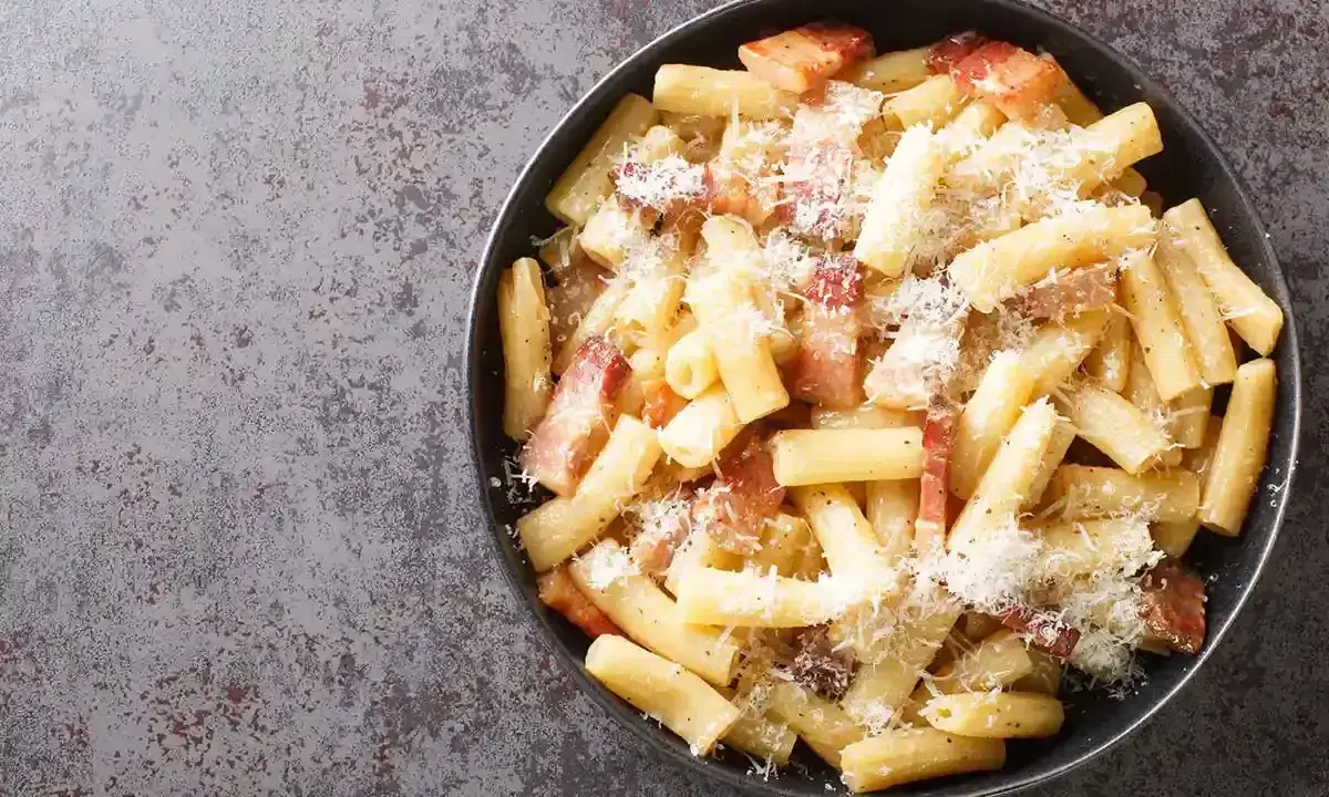 Un piatto di pasta alla zozzona fumante, con guanciale croccante e abbondante pecorino grattugiato, pronto per essere gustato.