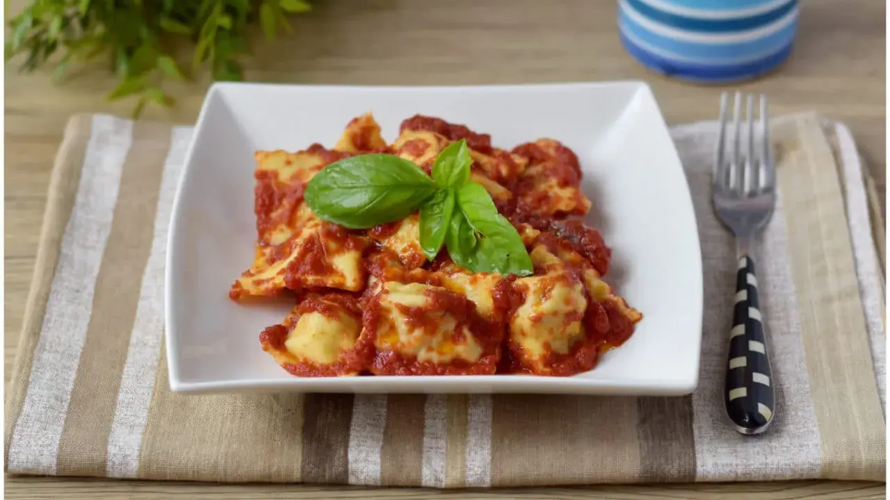 Un piatto di ravioli di carne conditi con sugo rosso e basilico fresco, pronti per essere gustati.