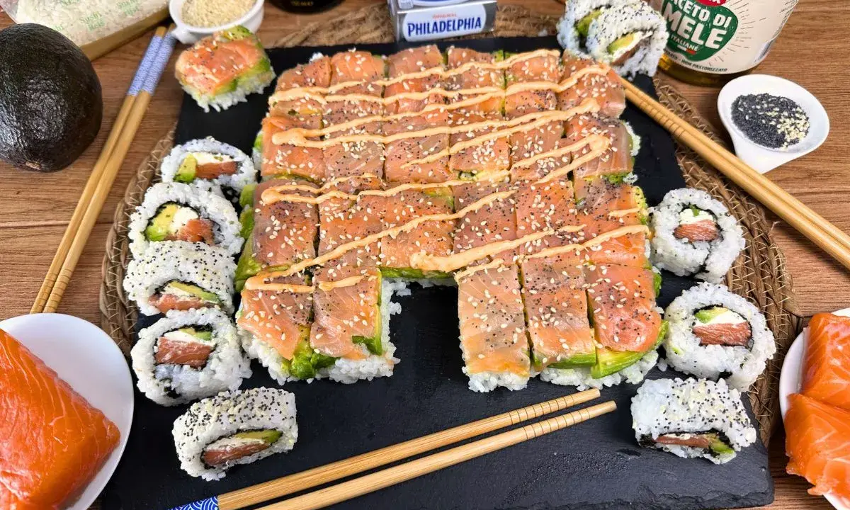 Un invitante sushi fatto in casa con salmone e avocado, guarnito con semi di sesamo e una salsa cremosa.