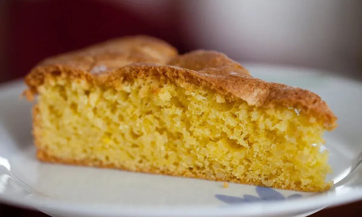 Una fetta di torta soffice e dorata, preparata con farina di mandorle, su un piatto bianco.