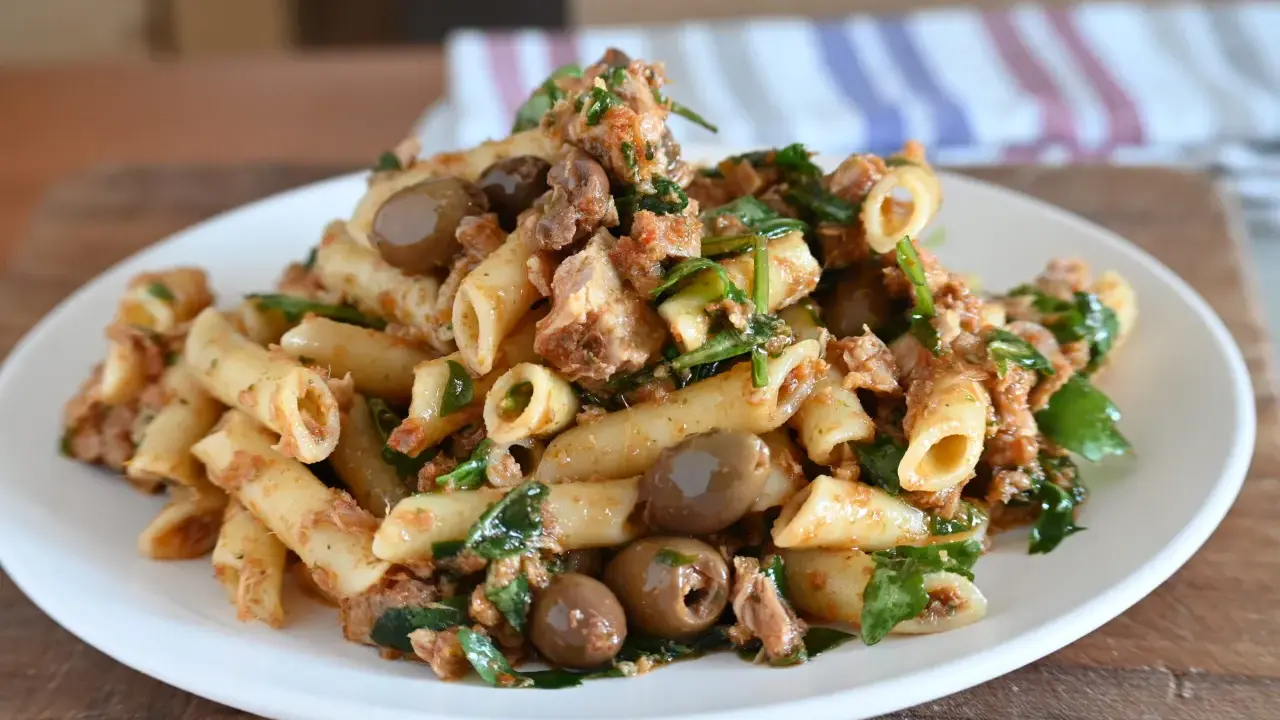 Piatto di pasta al tonno con olive verdi e prezzemolo fresco, servita su un piatto bianco.