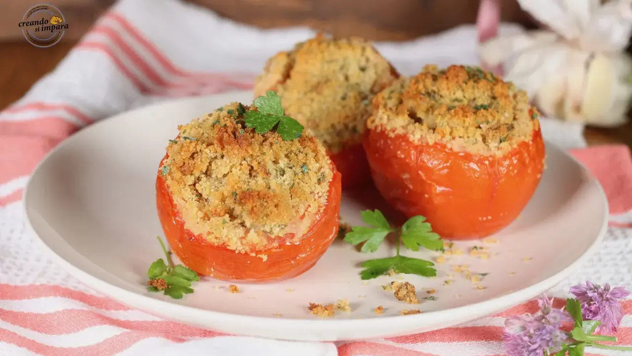 Tre pomodori gratinati al forno, ripieni e dorati, guarniti con prezzemolo fresco su un piatto bianco.