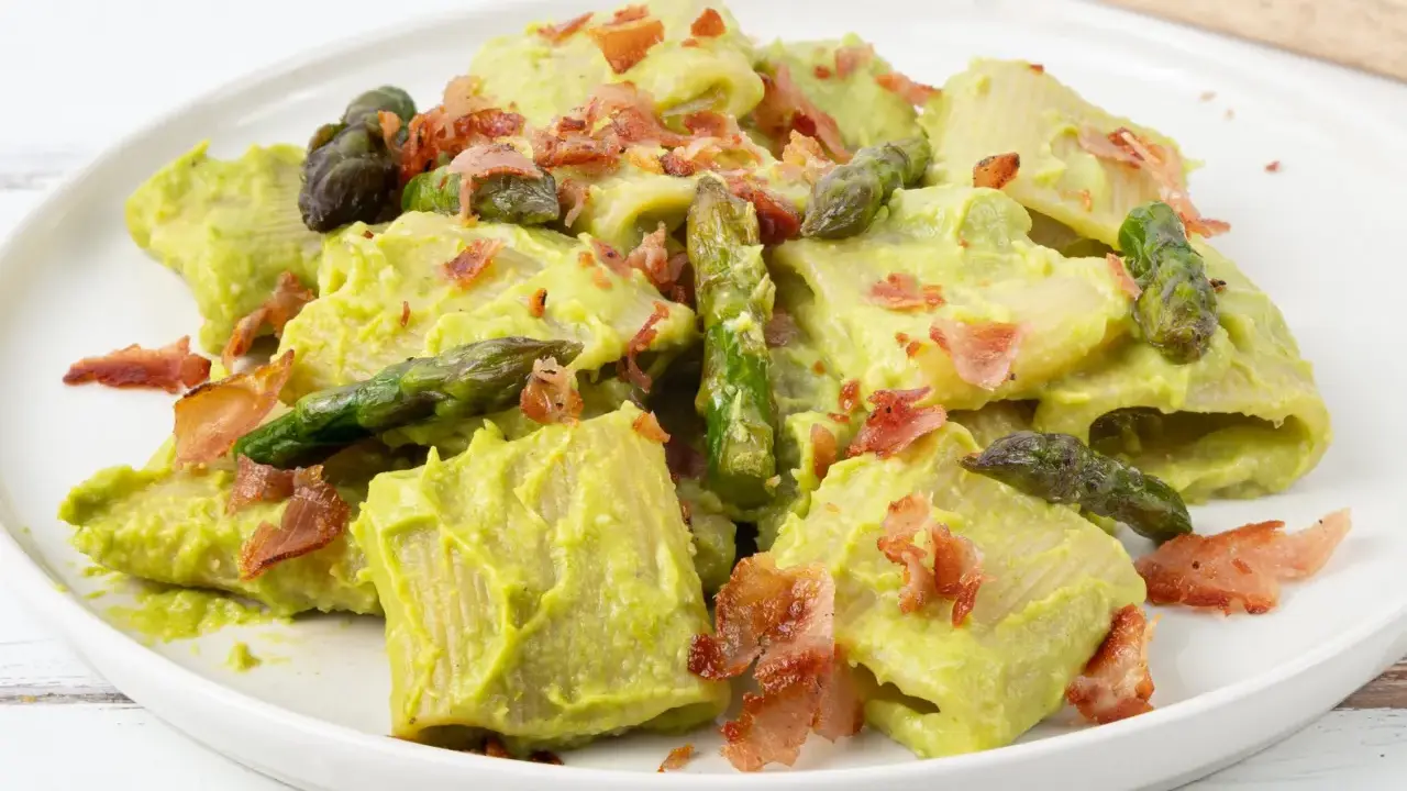 Piatto di pasta con crema di asparagi, punte di asparagi freschi e croccante speck.