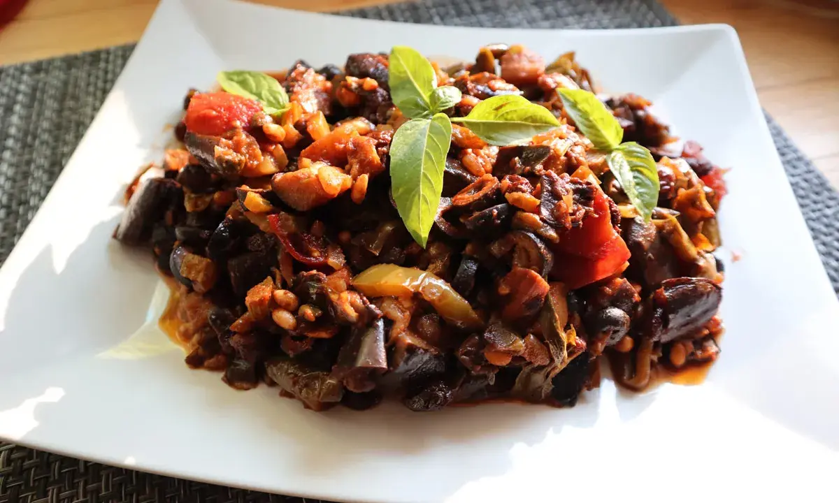 Un piatto di saporita caponata di melanzane, guarnita con foglie di basilico fresco.