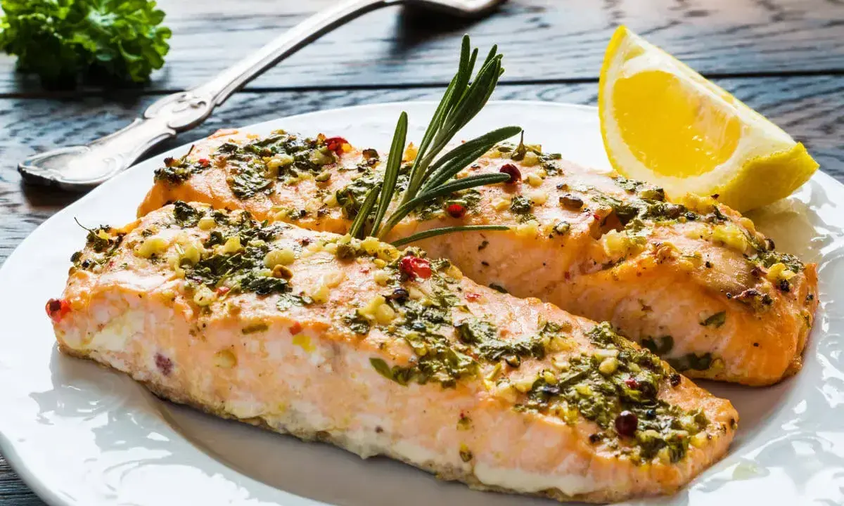 Delizioso salmone al forno con erbe aromatiche, aglio e peperoncino, guarnito con rosmarino e una fetta di limone.