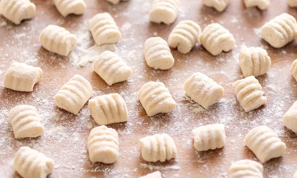 Gnocchi di ricotta freschi, pronti per essere cucinati, spolverati di farina su un tagliere di legno.