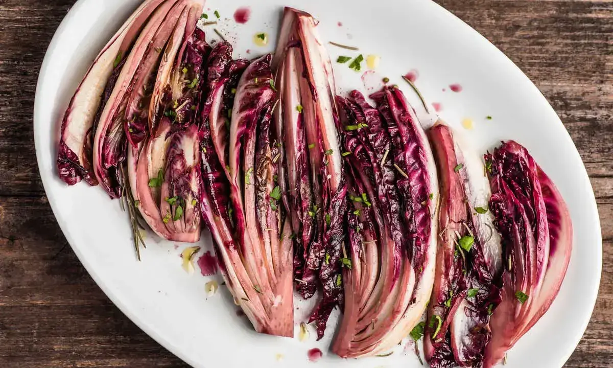 Radicchio al forno, tagliato a spicchi e condito con erbe aromatiche, servito su un piatto bianco.