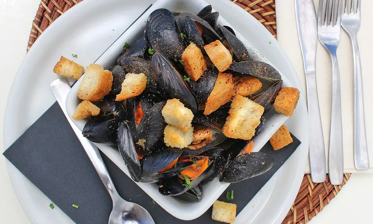 Un invitante piatto di impepata di cozze, ricco di molluschi neri e crostini dorati, pronto per essere gustato.