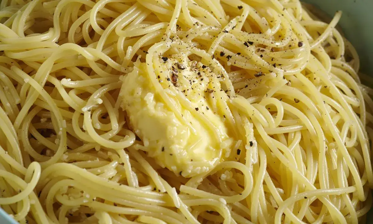Un piatto di spaghetti fumanti, conditi con burro fuso e pepe nero macinato fresco, un classico cacio e pepe pronto da gustare.