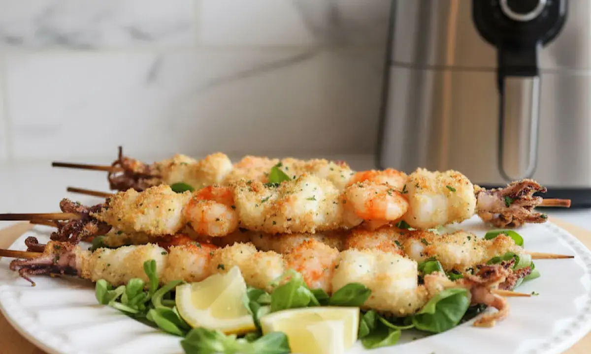 Spiedini di pesce croccanti, con gamberi e calamari impanati, serviti su un letto di insalata con spicchi di limone.