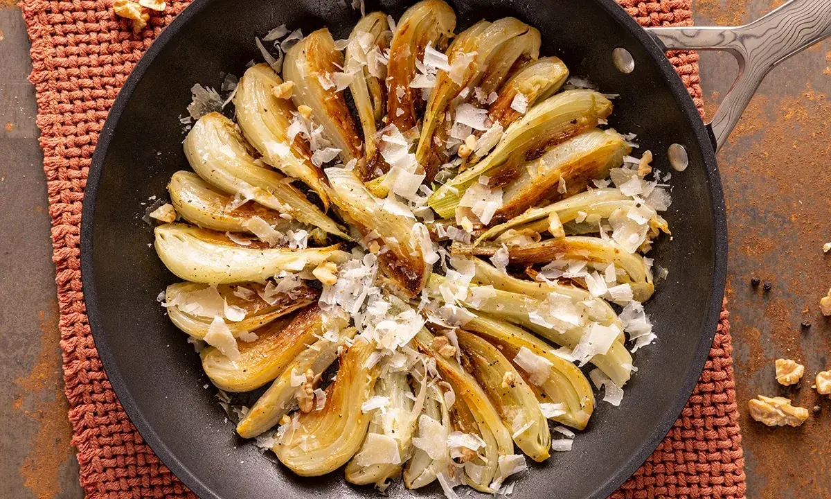 Finoçchi gratinati in padella, dorati e profumati, con scaglie di parmigiano e noci croccanti.