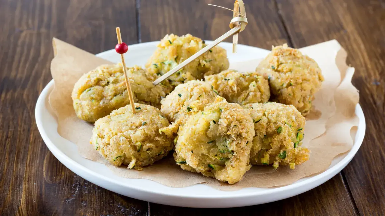 Polpette di ceci e zucchine dorate e croccanti, servite su un piatto bianco con stuzzicadenti decorativi.