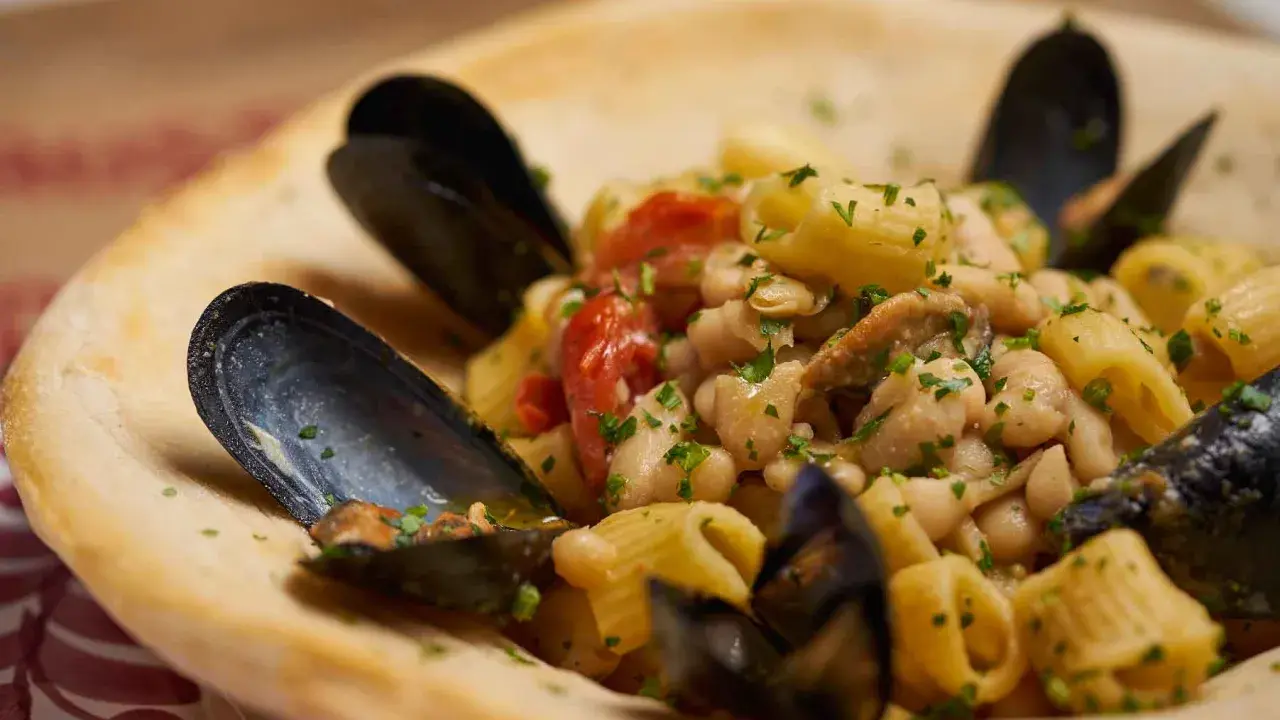 Un piatto invitante di pasta fagioli e cozze, con pomodorini e prezzemolo fresco, servito in una ciotola di pane croccante.