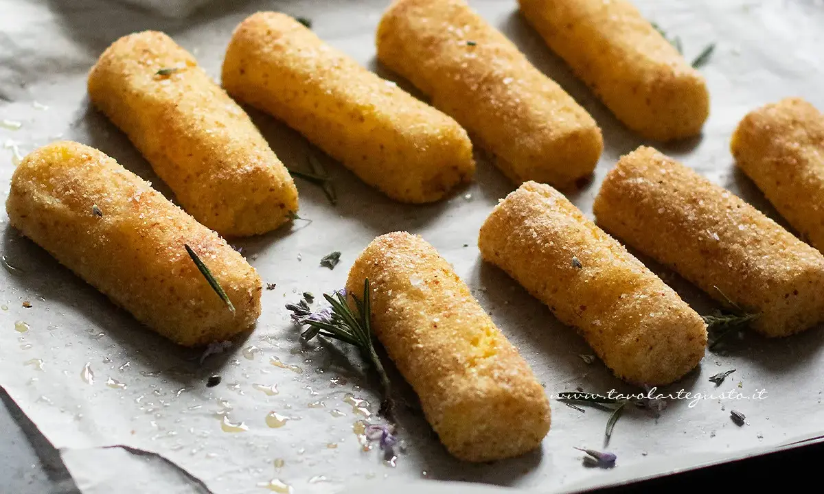 Crocchette di patate al forno dorate e croccanti, pronte per essere gustate. Profumate con rosmarino fresco.